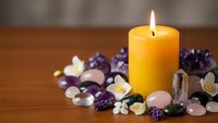 Burning yellow candle surrounded by colorful gemstones and crystals on wooden surface creating peaceful meditation and wellness atmosphere.