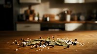 Scattered herbs and spices on wooden kitchen counter with blurred cookware and appliances in background, suitable for culinary and food styling projects.