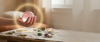 Young woman artist hand holding paintbrush creating artwork on wooden table with watercolor paints palette in bright sunlit studio workspace.