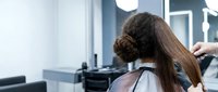 Professional hairstylist working on client's long brown hair in modern salon with styling tools and equipment for beauty treatments.