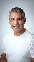 Confident middle-aged Hispanic man with gray hair smiling warmly in white t-shirt against neutral background for professional headshot or lifestyle content.