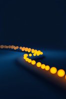 Glowing yellow lights create curved path against deep blue background, with soft bokeh effect producing dreamy, defocused illuminated spheres at night.
