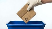 Gloved hand placing cardboard with recycling symbol into blue bin, promoting eco-friendly waste sorting and sustainable living habits.