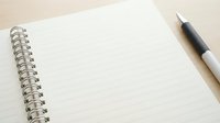 Open spiral notebook with blank lined pages and black pen on wooden desk surface for writing notes and planning tasks.