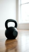 Black kettlebell weight on wooden floor near bright window, suitable for fitness, gym, strength training, and workout design projects.