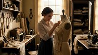 Female tailor working on dress form in traditional sewing workshop with vintage tools and natural lighting from window creating authentic craftsmanship atmosphere.