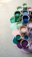 Colorful paint cans with spilled paint creating vibrant puddles on concrete floor for home renovation and interior design projects.