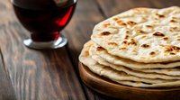 Stack of fresh homemade flatbread naan on wooden cutting board with red wine glass in background on rustic wooden table. Traditional Indian cuisine.