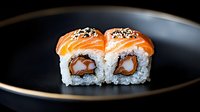 Fresh salmon sushi rolls with cream cheese and black sesame seeds served on black ceramic plate against dark background, close up view of Japanese cuisine.