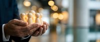 Senior businessman cupping hands with glowing light bulbs representing innovative ideas and creative solutions in modern office environment.