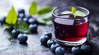 Fresh blueberry juice in glass with ripe berries and mint leaves on dark stone background, healthy antioxidant drink for detox and wellness.