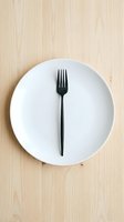 Empty white plate with black fork centered on light wood surface, representing fasting, dieting, minimalism, and healthy eating concepts for nutrition and wellness design projects.