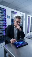 Middle-aged Caucasian male IT professional in business attire analyzing digital data on tablet in server room with purple-lit server racks.