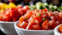 Fresh diced tomatoes with chopped herbs in white ceramic bowl, close up view of homemade salsa ingredients. Vibrant red tomato chunks garnished with green onions.