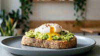 Avocado toast with poached egg on whole grain bread, served on a gray plate in a modern cafe setting.
