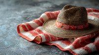 Straw sun hat with red decorative band placed on striped cotton towel against textured gray background, creating rustic summer vacation mood.