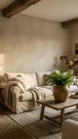 Rustic farmhouse living room with cream upholstered sofa, wooden beams, terracotta plant pot with greenery, and neutral textured walls for home decor inspiration.