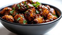 Glazed meatballs with fresh herbs in black bowl, savory appetizer dish for restaurant menu, cooking blog, food photography and culinary presentations.