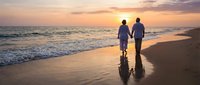 Romantic couple walking hand in hand on beach at sunset with golden sky and ocean waves reflecting on wet sand creating peaceful evening atmosphere.