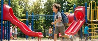 Young African American boy playing on colorful playground equipment with slides and climbing structures in sunny park setting for active childhood recreation.