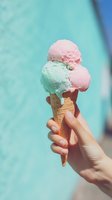 Hand holding waffle cone with pink and mint ice cream scoops against turquoise background, perfect for summer food marketing.