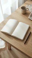 Open blank notebook with pen and coffee mug on wooden desk in bright natural light creating peaceful workspace atmosphere for writing and planning.
