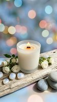 White scented candle with flame on rustic wooden board decorated with small white roses and smooth stones against soft bokeh lights background for spa relaxation.