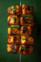 Grilled chicken kebab with fresh herbs and spices on metal skewer against dark green background, close up view of juicy marinated meat cubes.