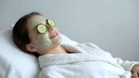 Young woman relaxing with green facial mask and cucumber slices on eyes during spa treatment. Natural skincare and wellness routine concept.