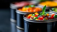 Fresh colorful vegetables and herbs in black containers, selective focus on cherry tomatoes, corn and mint leaf, showcasing healthy meal prep and catering service.