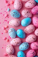 Colorful speckled Easter eggs in pink and blue tones arranged on pink background with scattered candy pieces for festive holiday celebration.