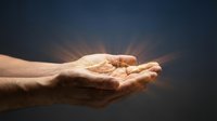 Male hand with open palm facing upward against dark background with golden light rays emanating from above, symbolizing spirituality, hope, and giving for religious or motivational content.