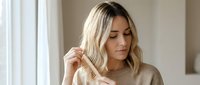 Young blonde woman combing her wavy hair with wooden comb in bright bathroom, morning haircare routine, natural beauty and wellness lifestyle.