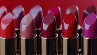 Row of luxury lipsticks in various shades of red and pink with metallic gold cases against dark background, showcasing cosmetic product range for beauty industry.