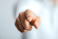 Close-up of African American hand pointing finger directly at viewer against blurred white background, selective focus on fingertip for business concept.