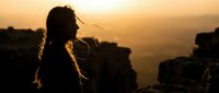 Young woman silhouette with flowing hair against golden sunset sky, peaceful moment of contemplation and freedom in nature during golden hour.