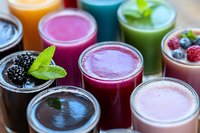 Fresh colorful smoothies and juices in glass jars garnished with berries and mint leaves, healthy detox drinks with vibrant purple, green, pink and orange hues.