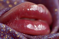 Close up of glossy red lips with shimmering glitter makeup details against blurred bokeh background, showcasing glamorous beauty and cosmetic artistry.