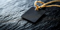 Black blank price tag with twine string on dark stone background, dramatic lighting creates moody atmosphere for retail and marketing designs.