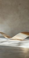 Elegant beige silk ribbon curves gracefully on white surface with soft shadows and neutral background, creating minimalist composition for luxury branding.