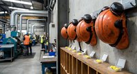 Industrial safety helmets hanging on wall in manufacturing facility with workers in background for workplace protection concepts.