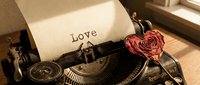 Vintage typewriter with the word Love typed on aged paper, adorned with a dried red rose, evoking romance and nostalgia.