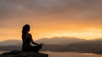 Woman silhouette meditating in lotus pose at sunset with mountain landscape background. Peaceful yoga practice for mindfulness and spiritual wellness.