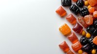 Colorful gummy candies arranged on white background, including black, orange and red fruit-flavored jellies with sugar coating, creating decorative border pattern.