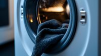 Closeup view of washing machine door with dark blue towel inside, illuminated by warm interior light creating moody laundry room atmosphere.