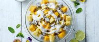 Tropical mango chia seed pudding bowl with coconut yogurt and fresh mint leaves on white wooden background for healthy breakfast recipe.