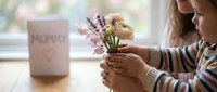 Child holding spring flowers with Mother's Day card on table celebrating family love and appreciation.