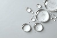 Clear water drops on white surface, macro photography showing transparency and purity of liquid bubbles with light reflection.