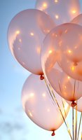 Soft pink balloons with glowing light reflections against blue sky background create magical festive atmosphere for celebration and party decoration.