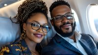 Young African American couple smiling while traveling by private jet, wearing glasses and business attire, expressing joy and success during luxury air travel.